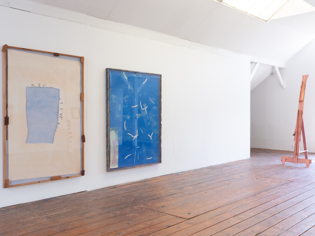 Two large abstract drawings in blue and cream mounted on the wall, with a pink easel-like sculpture nearby.