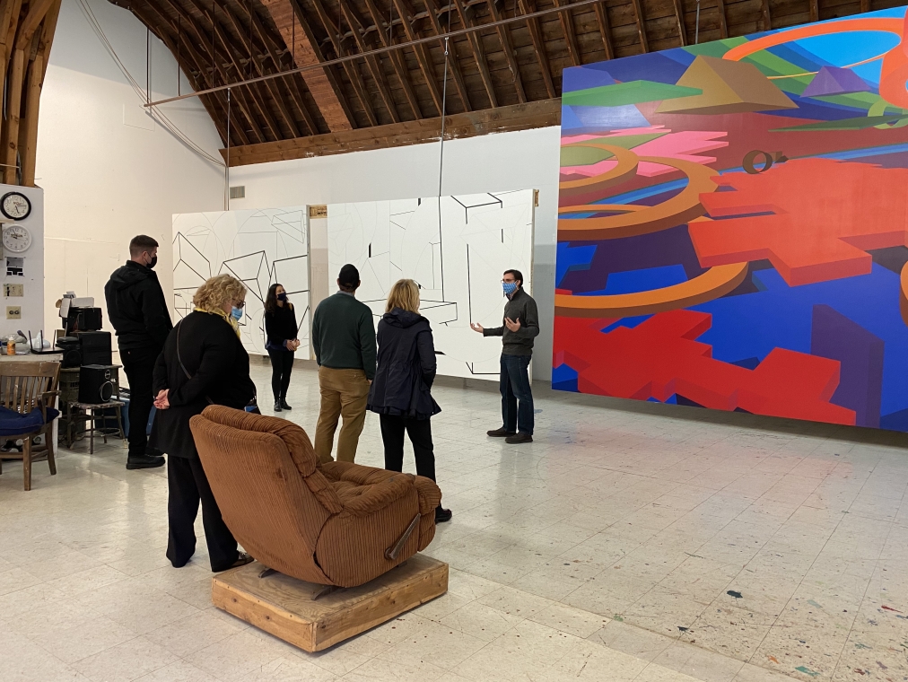 Group of people gathered in Al Held's former painting studio, looking up at three very large scale abstract acrylic paintings by Held.