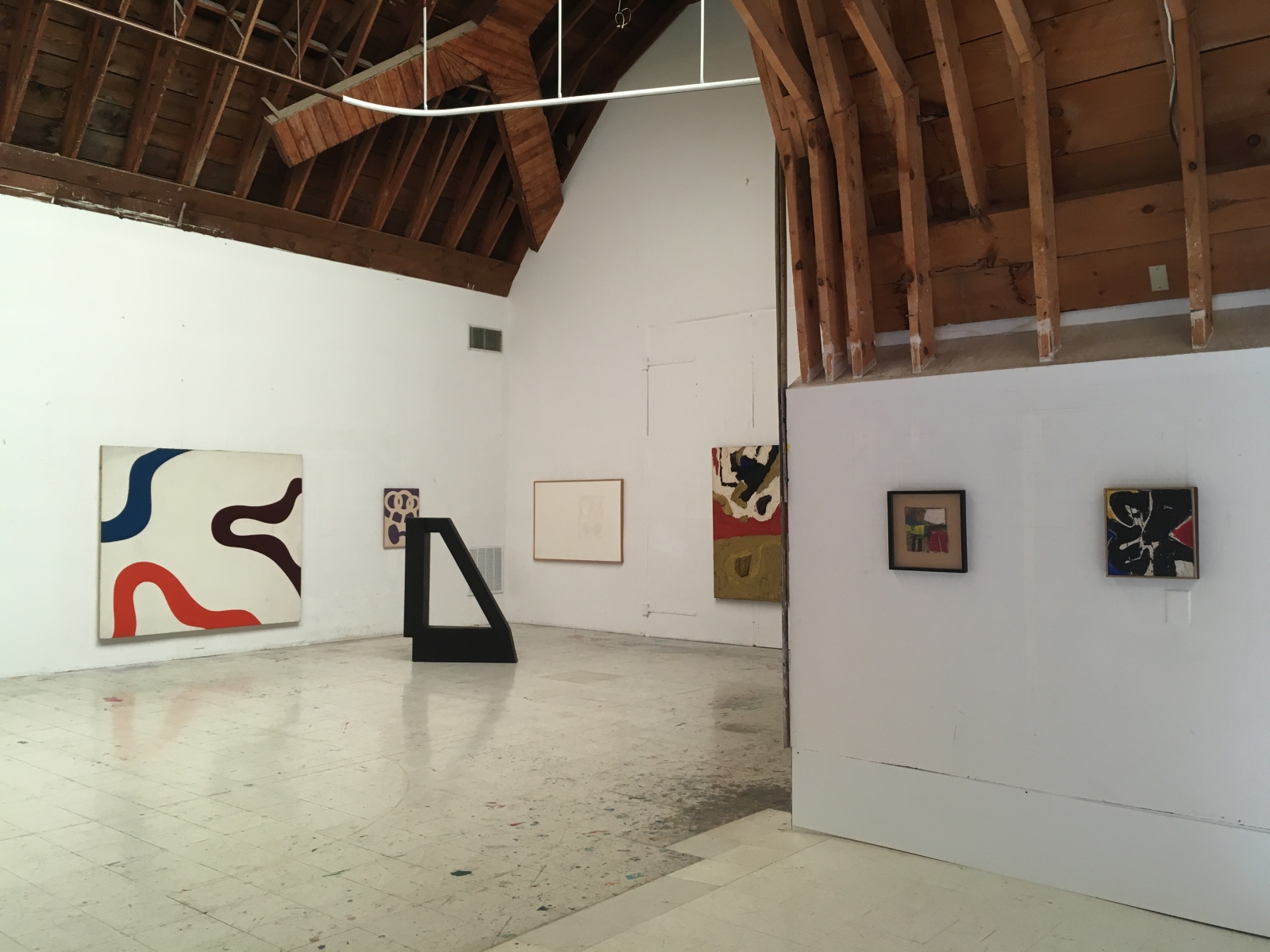 Installation view of six abstract paintings and one black minimalist geometric sculpture.